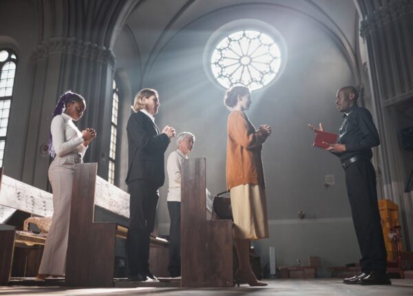 Group of people standing and praying during mass together with priest in the church